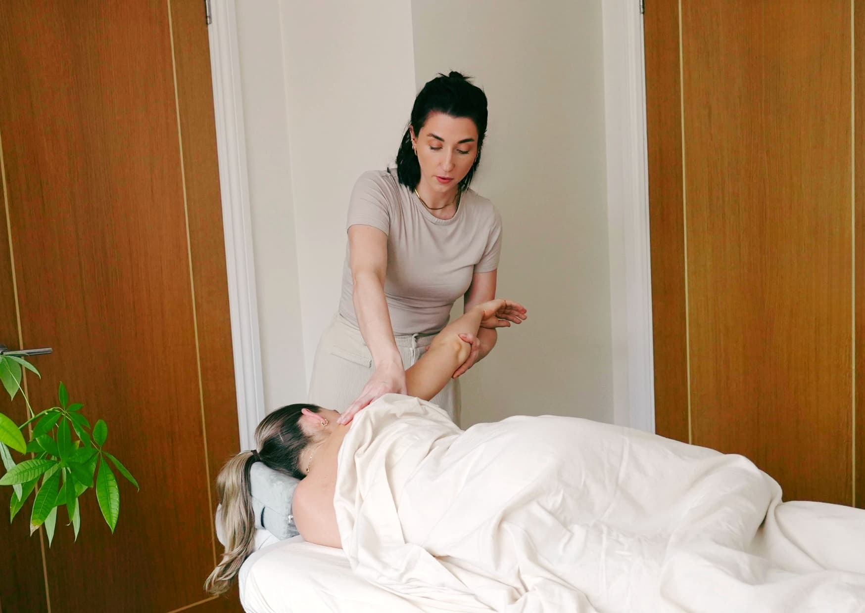 Rebecca treating a client's shoulder on a treatment couch, with a plant beside it